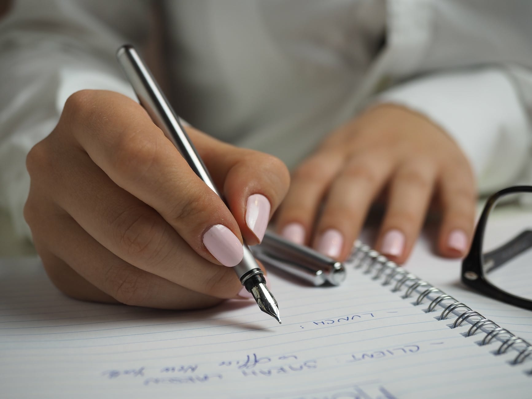 woman in white long sleeved shirt holding a pen writing on a paper. smart money bro