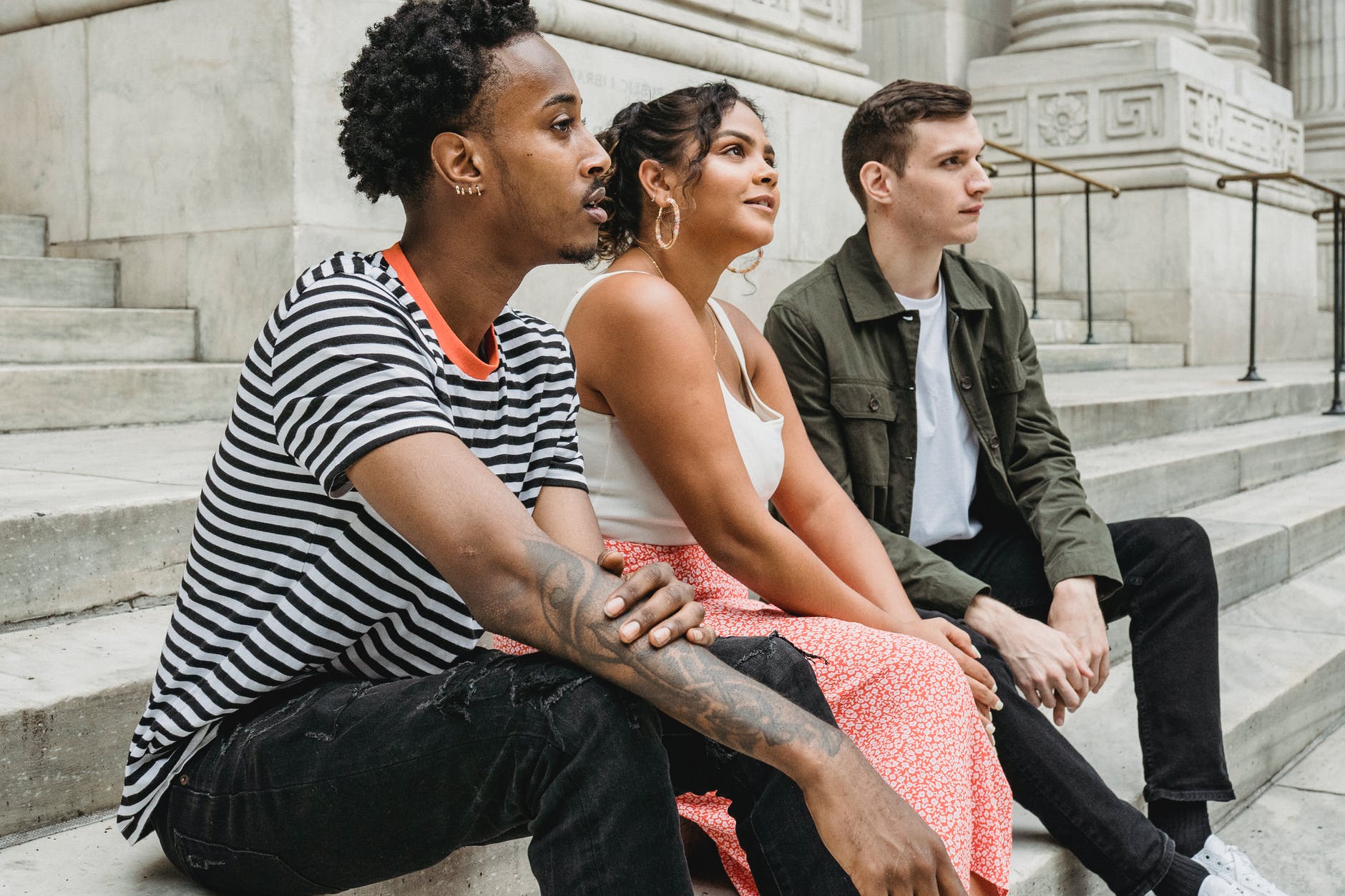 multiracial friends sitting on stairs near building in street