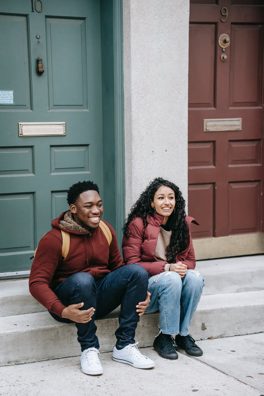 multiethnic cheerful friends smiling on gray stairs of building