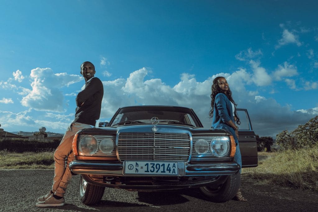 stylish black couple standing near retro car in countryside