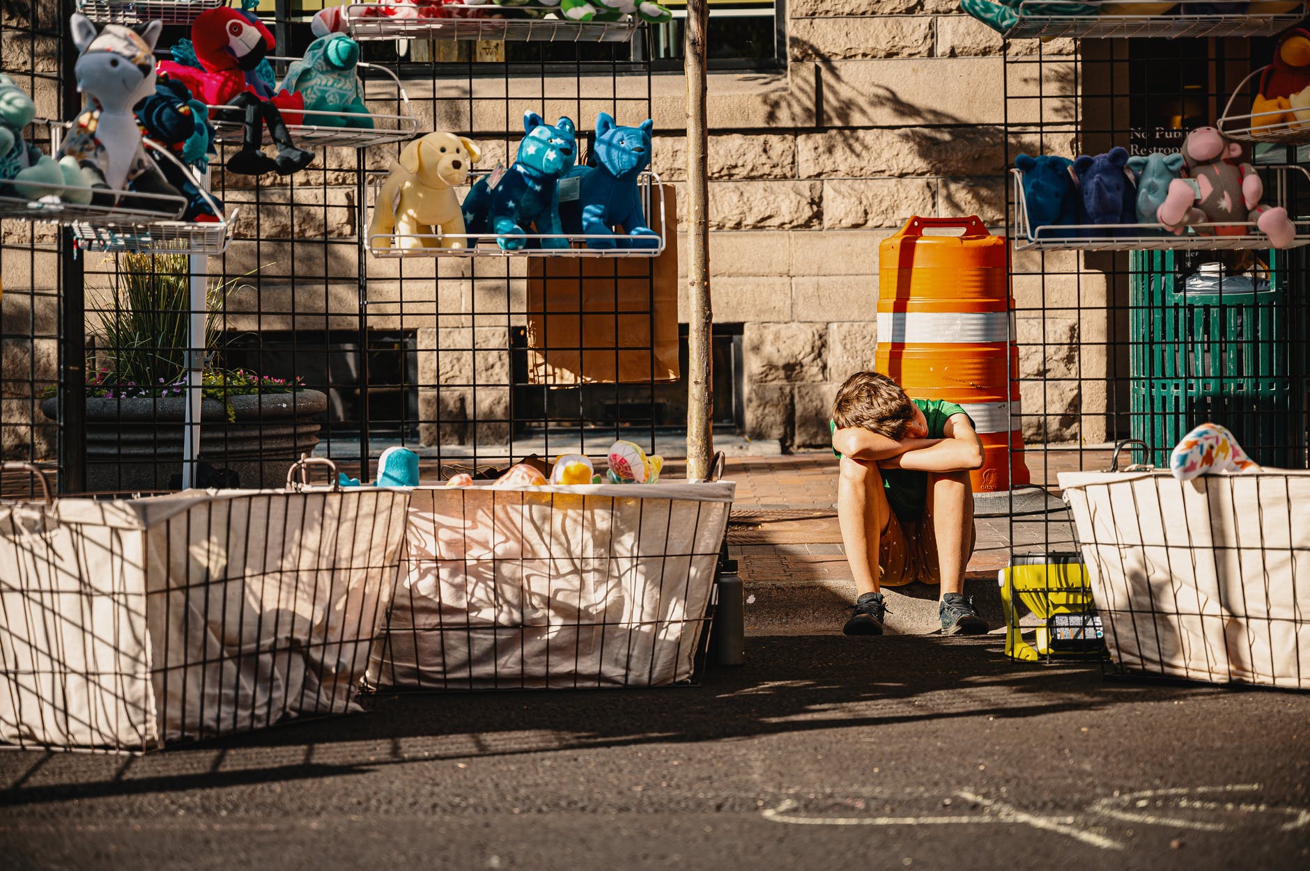 boy crouching and resting head on hands and knees between shelf of plush toys, smart money bro