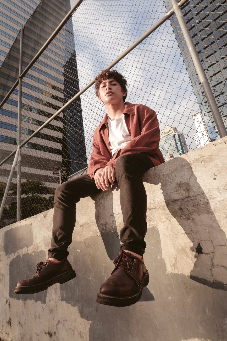 man in red polo shirt sitting on brown concrete wall, smart money bro