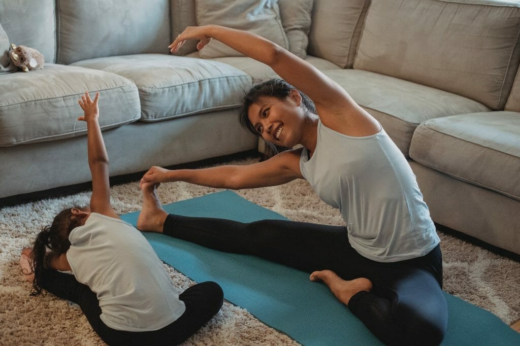 cheerful asian mother and daughter stretching body in living room