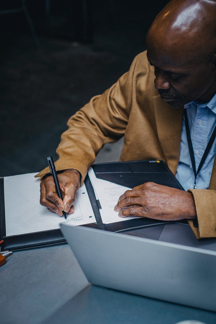 crop concentrated black man taking notes in documents, smart money bro