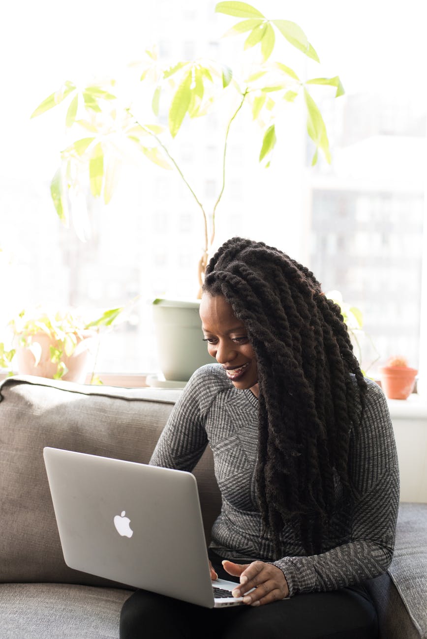 woman sittin on gray couch while holding her apple macbook air, ways to be different with money